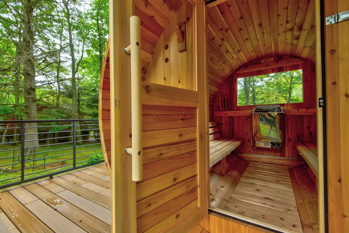 A serene interior shot of the wooden sauna featuring large windows that frame the lush outdoors. The benches and soft lighting evoke a calming, wellness-focused retreat.