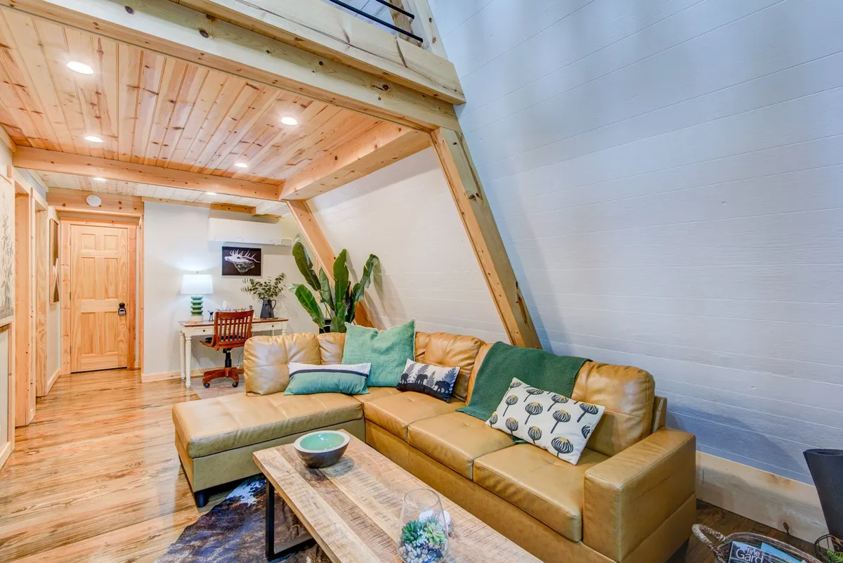 A welcoming living room featuring a sofa, a wooden coffee table, an integrated work desk area, and green plants. The arrangement allows for both relaxation and productivity, embodying a sense of versatility and comfort.