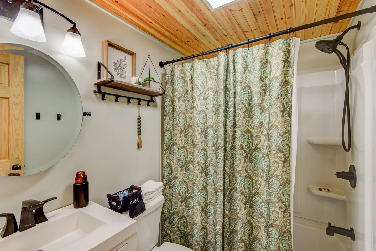 A serene bathroom space with a round mirror, decorative shower curtain, and a shelf with plants. The calming decor creates a spa-like atmosphere, perfect for morning routines or unwinding after a day of play.