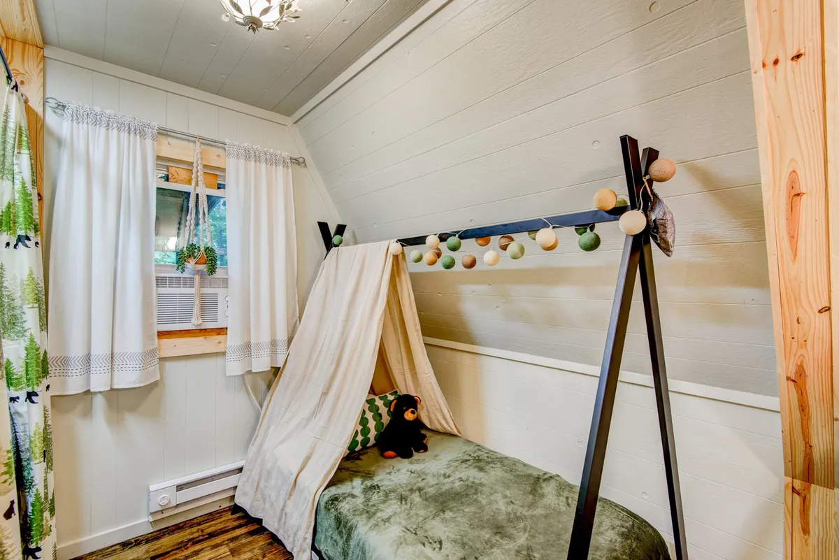 A whimsical and playful children’s bedroom featuring a bed draped with decorative curtains and strung with twinkling string lights. The cozy setup evokes the atmosphere of a teepee or tent, ideal for imaginative play and restful sleep.