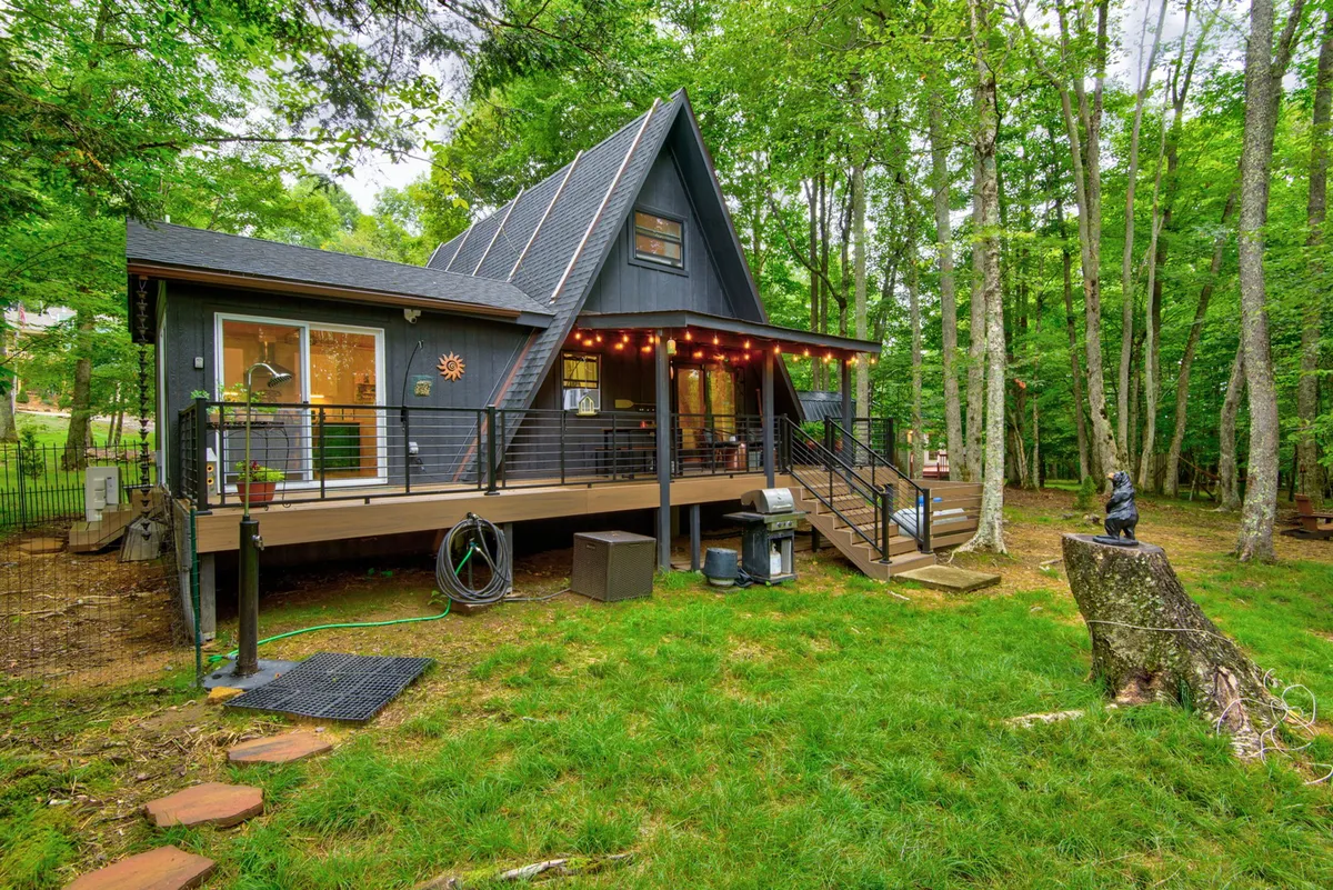 An inviting exterior shot of the A-frame home’s deck, adorned with string lights and surrounded by trees. The deck includes railings, and its proximity to nature suggests a secure yet open area for both pets and owners to enjoy. The ambiance is cozy and welcoming, perfect for evening relaxation after daytime exploration with pets.