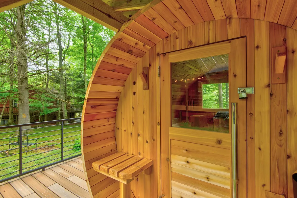A cozy wooden sauna with a glass door that frames views of surrounding greenery. Warm wooden benches invite guests to relax and immerse themselves in a calming, rejuvenating atmosphere closely connected to nature.