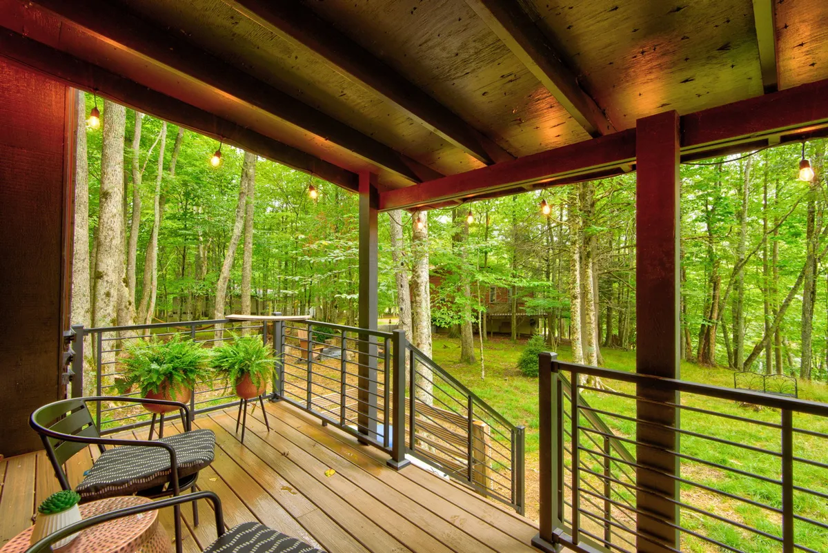 A tranquil exterior seating area surrounded by trees, featuring a wooden railing and hanging lights. The inviting space is perfect for relaxing, reading, or enjoying the peaceful ambiance of nature, with sunlight streaming through the leaves.
