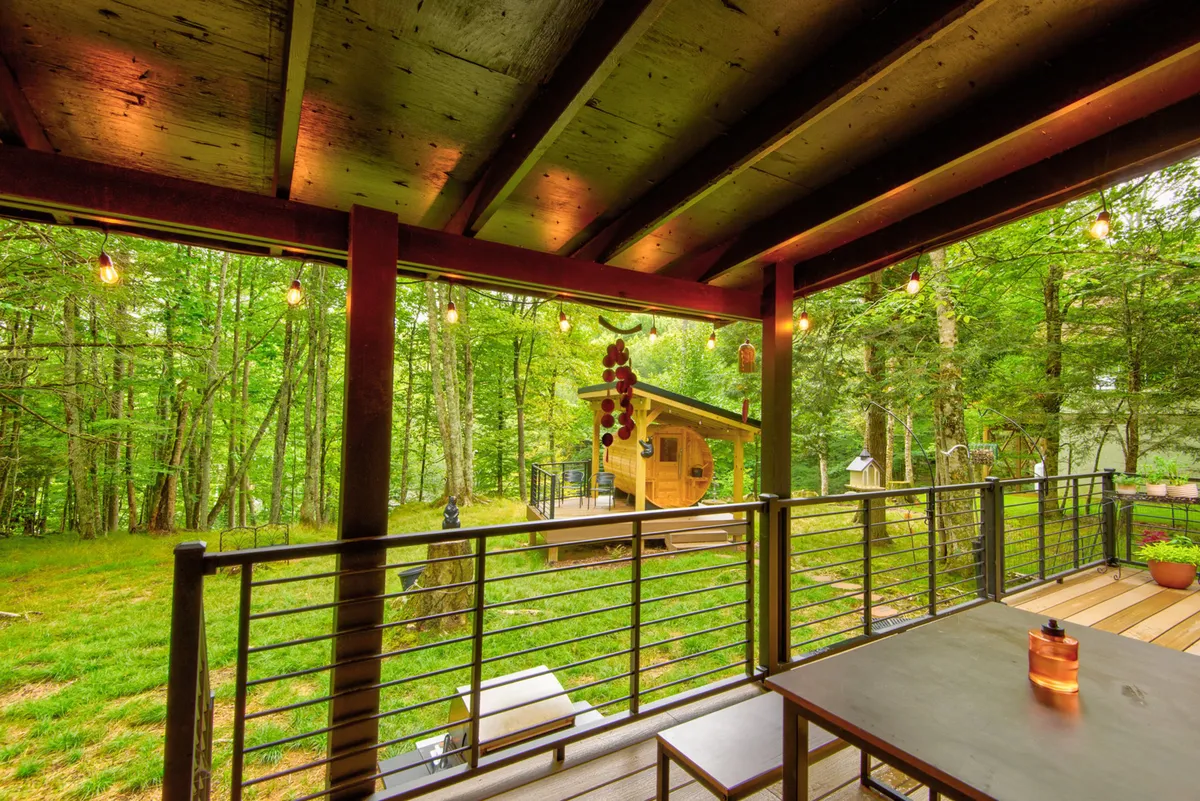 This exterior image features a charming wooden cabin adorned with string lights and a welcoming outdoor dining table, situated in a serene natural setting. The scene evokes a sense of community and relaxation, with plenty of space for guests to gather for meals or socialize under the stars.
